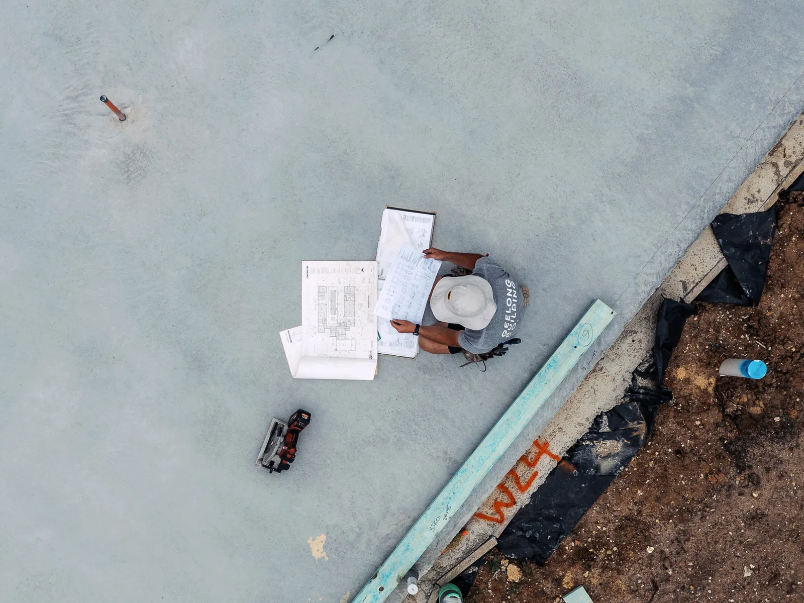Aerial view of a builder reading plans on a freshly poured slab